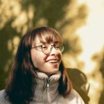Portrait of a young woman with glasses enjoying sunlight outdoors, capturing a joyful moment.